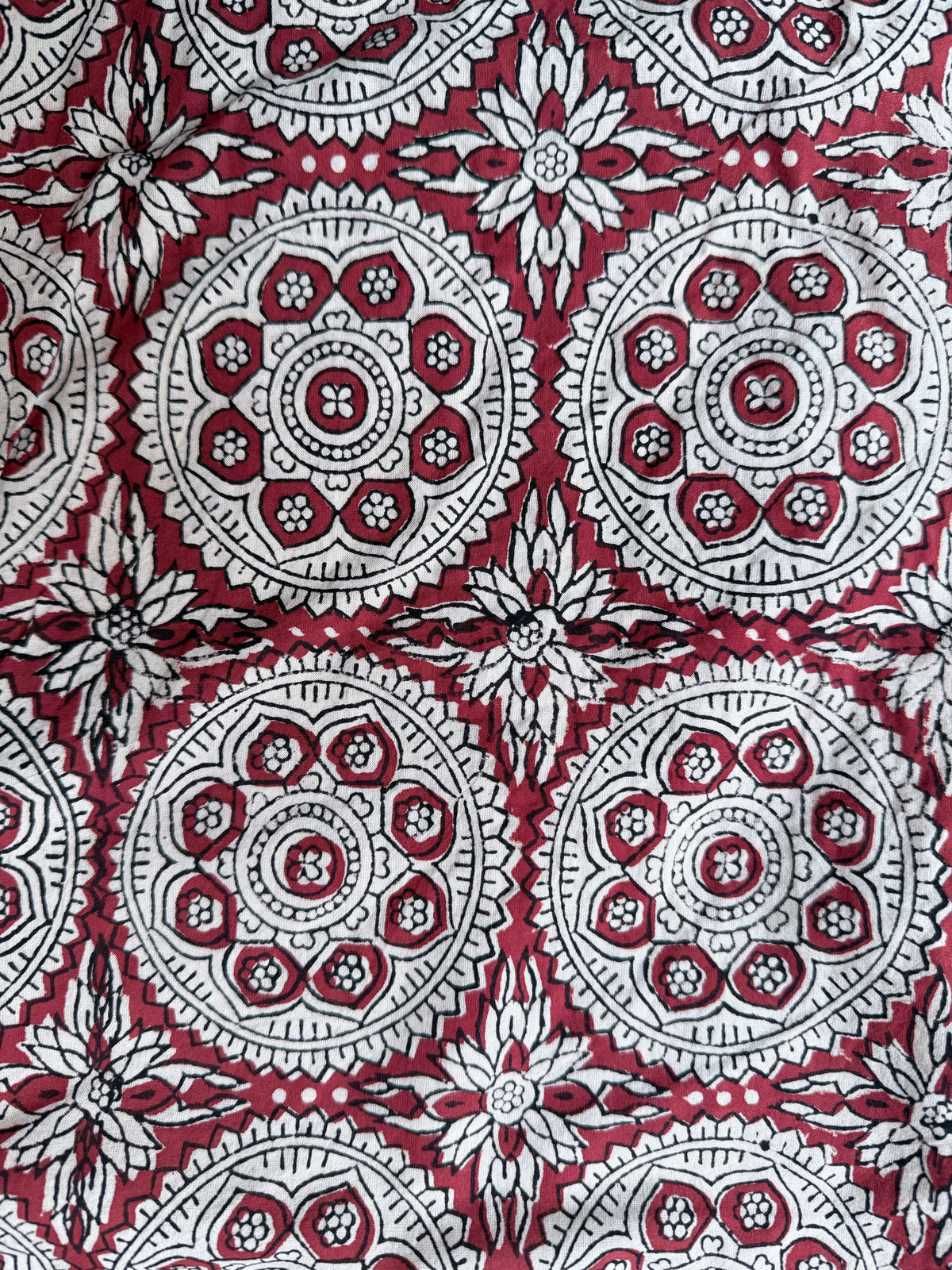 A close-up of a fabric pattern featuring circular mandala and floral motifs in red, white, and black.